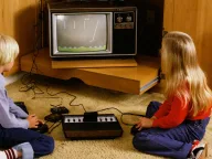 Two children playing an Atari VCS games console on a wood-panelled television cabinet, early 1980s