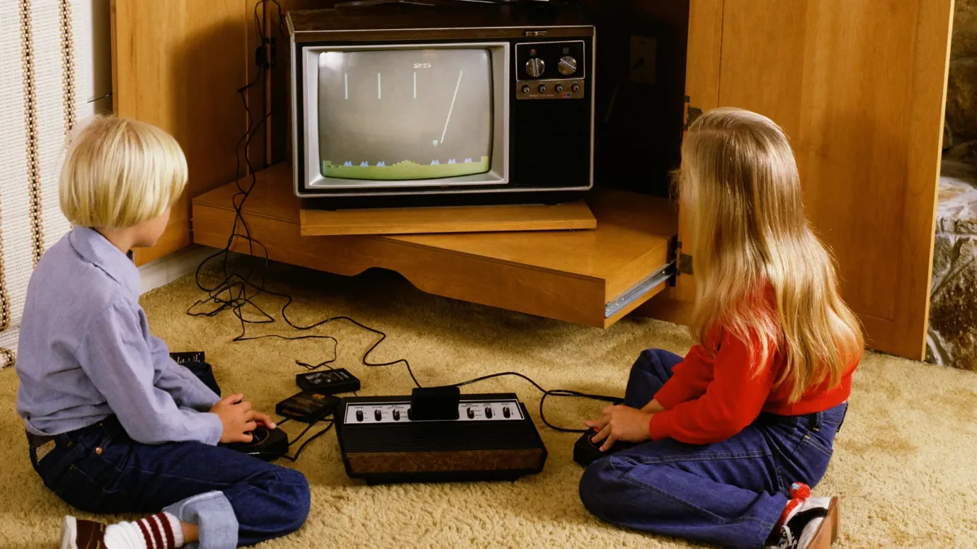 Two children playing an Atari VCS games console on a wood-panelled television cabinet, early 1980s