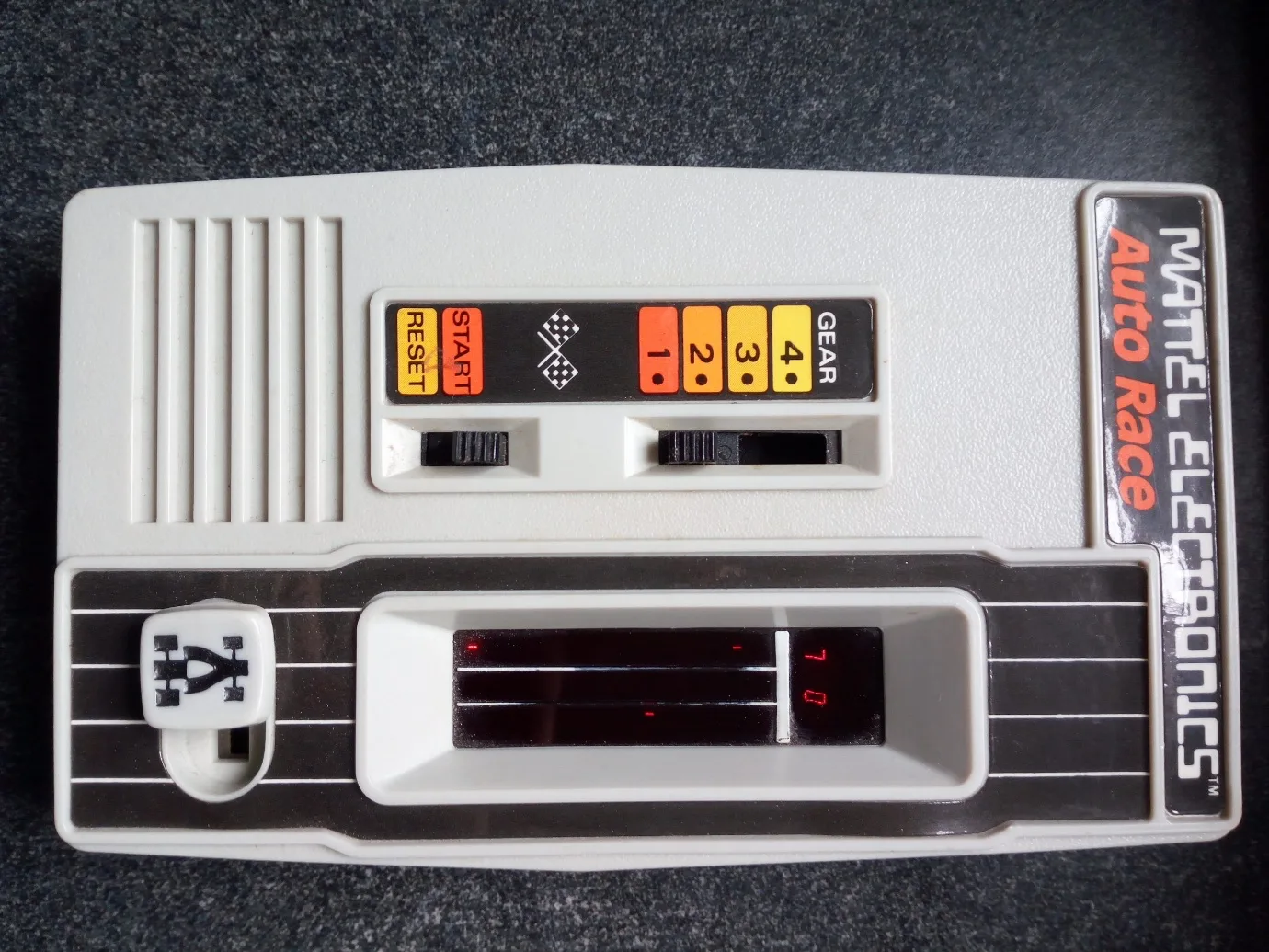 Top-down view of the Mattel Auto Race handheld, showing the gear switch, start/reset sliders and the three-lane LED track