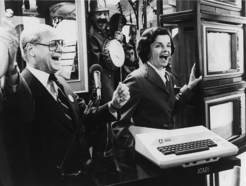 Press event with an Atari 800 on the podium, laughing crowd and a banjo player behind